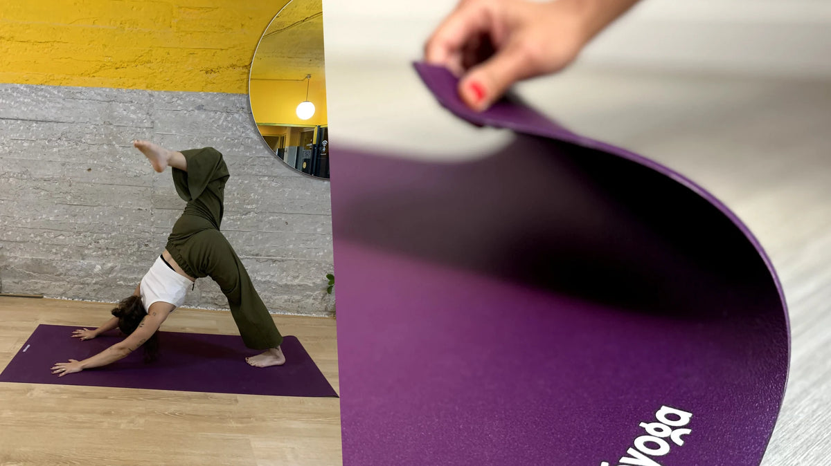 A three-legged downward dog on a purple yoga mat, and a hand lifting the corner to show its thickness