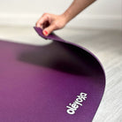 Hand lifting a corner of the Deep Purple oléyoga mat to show how flexible it is