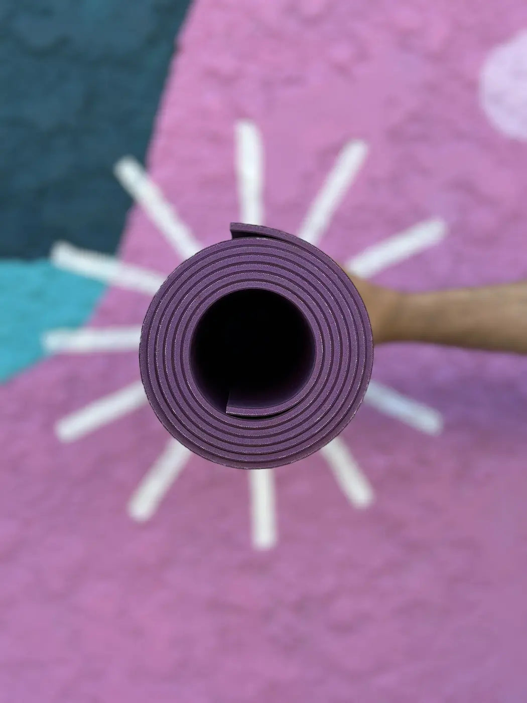 Rolled oléyoga yoga mat in front of a mural