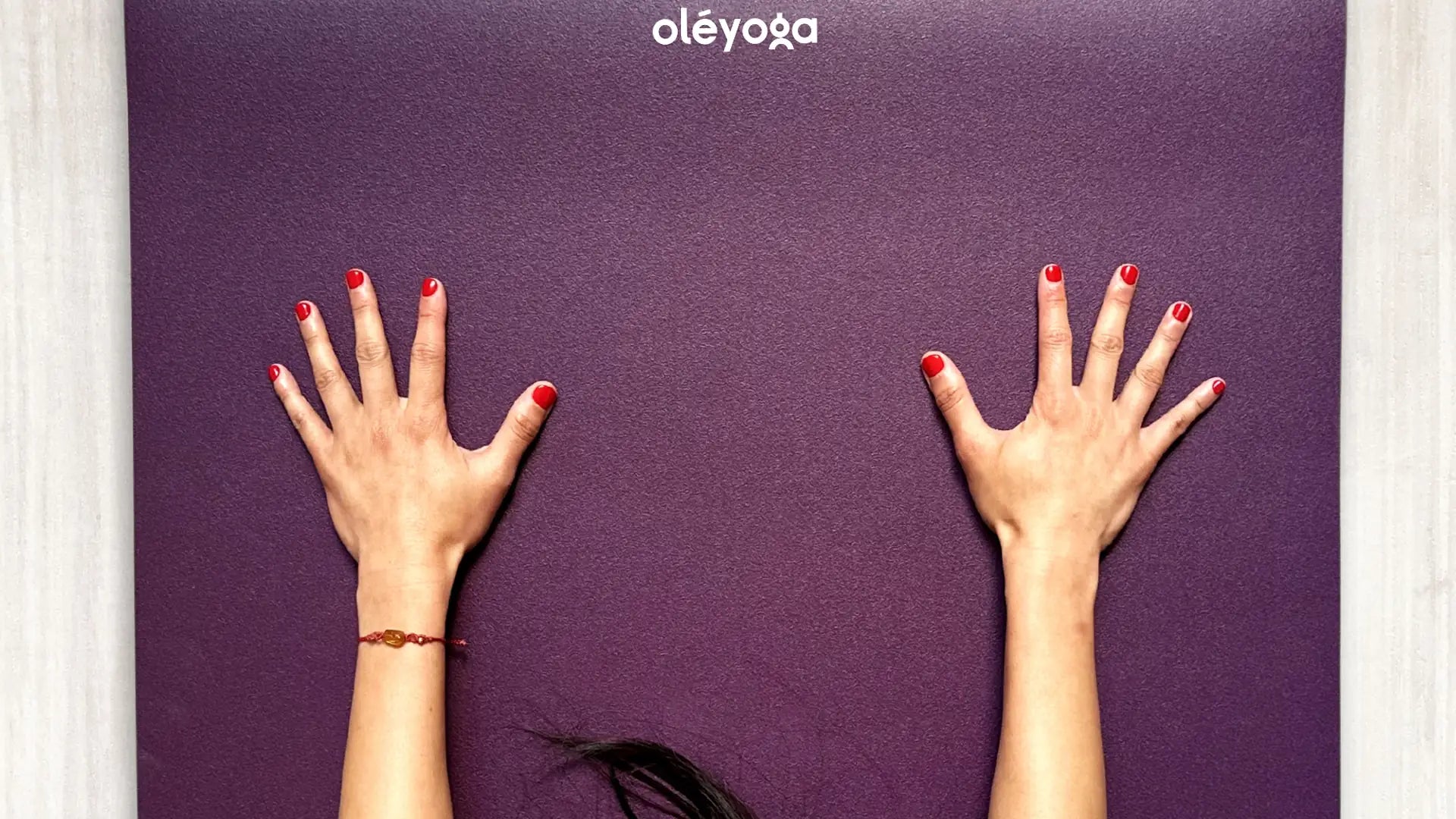 Two hands with spread fingers pressing down on a purple natural rubber yoga mat, seen from directly above.