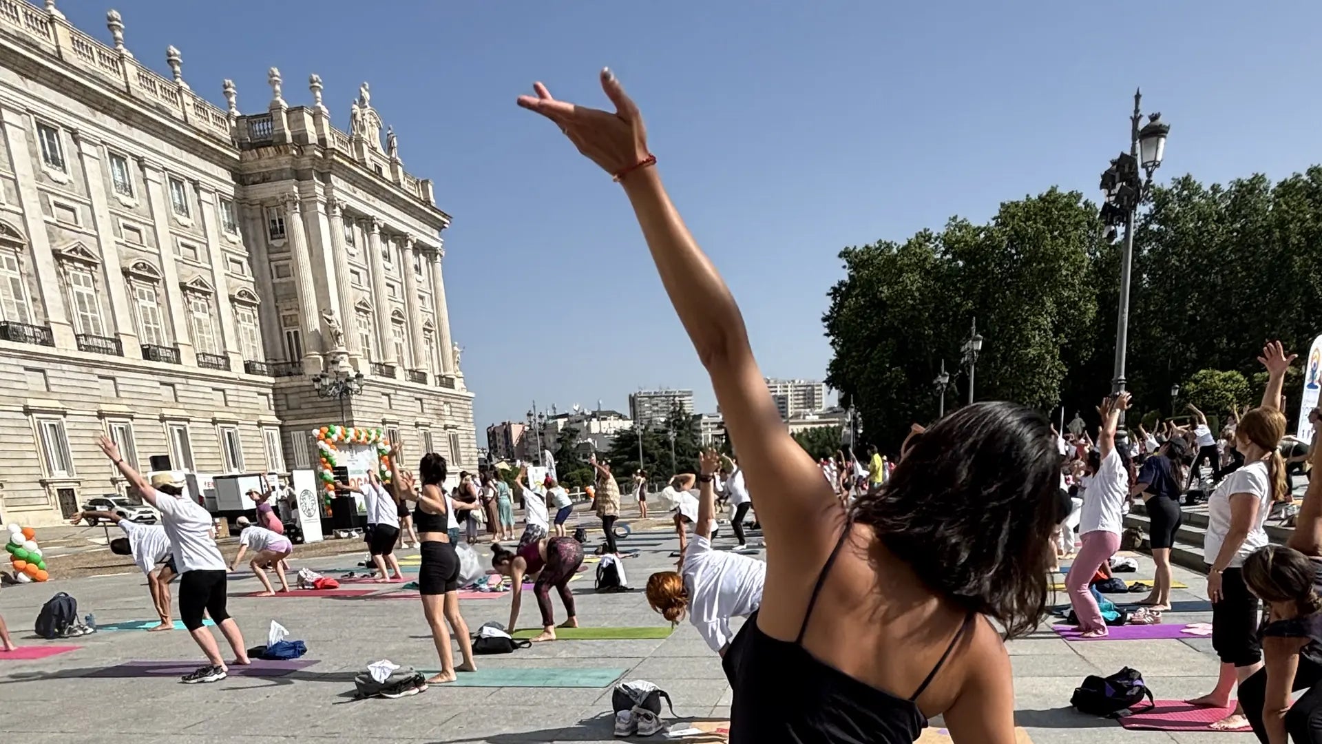 Open-air yoga class on mats in front of the Royal Palace in Madrid, one practitioner with an arm raised