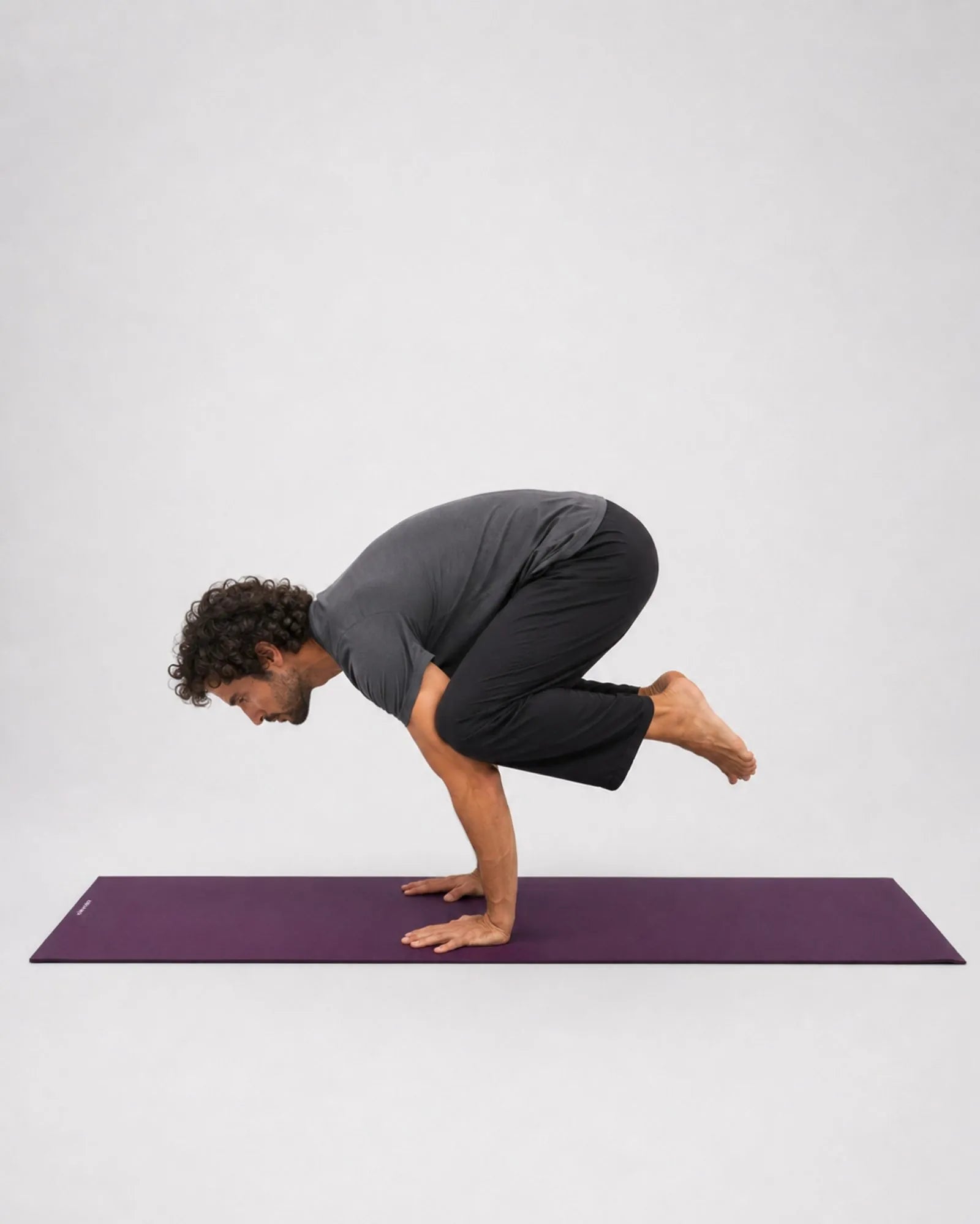 Practitioner in crow pose with hands on a purple natural rubber yoga mat