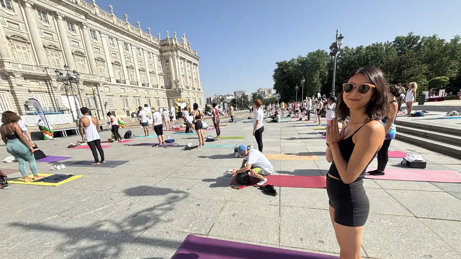 Practitioner standing in prayer on a purple mat at an open-air mass yoga class in front of the Royal Palace in Madrid